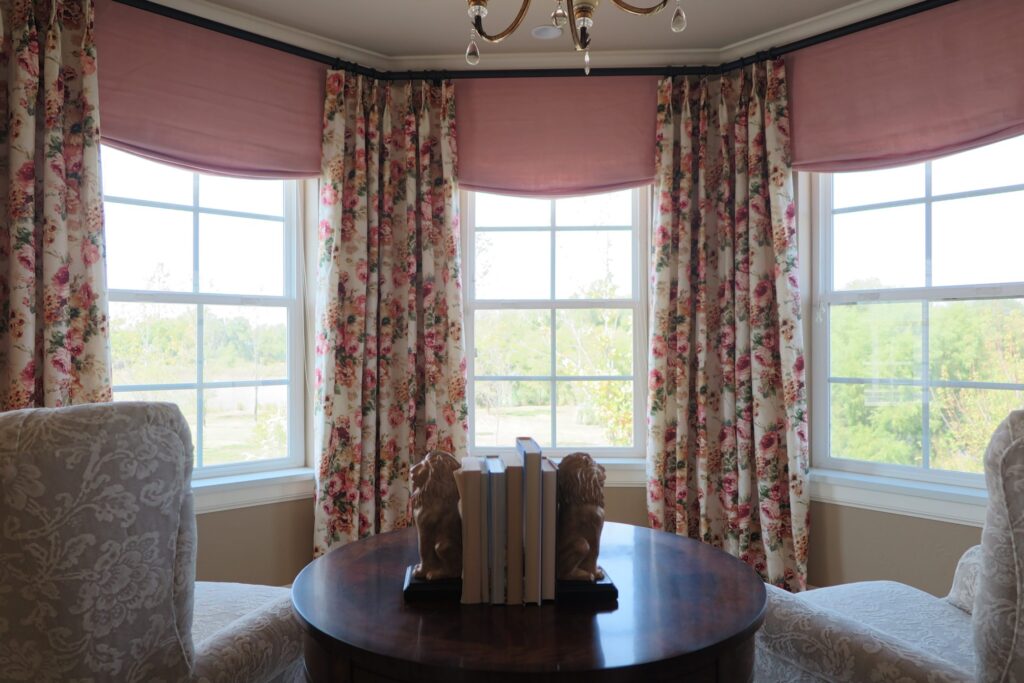 A cozy room with a table and chairs by a window with floor to ceiling custom rose floral curtains