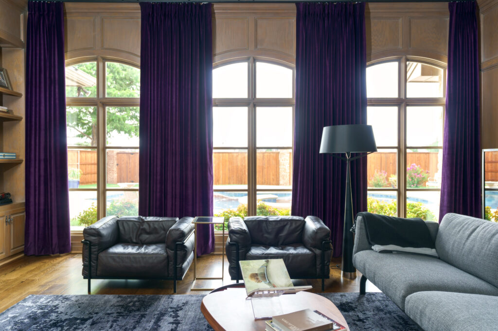 A stylish living room with purple curtains and sleek black leather furniture.