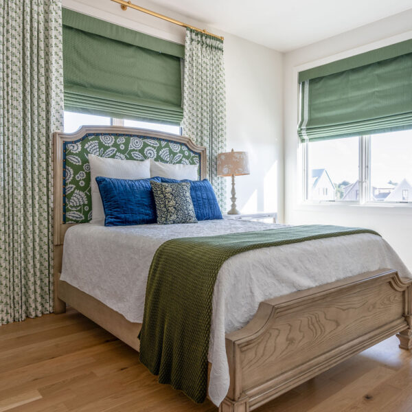 A cozy bedroom with fresh sage and olive green with white bedding, complimented by striking curtains accented with same toned coloration all illuminated by natural light from a window.