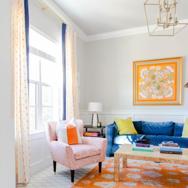 A modern living room decorated with eye-catching orange and blue furniture and sheer high-end draperies..