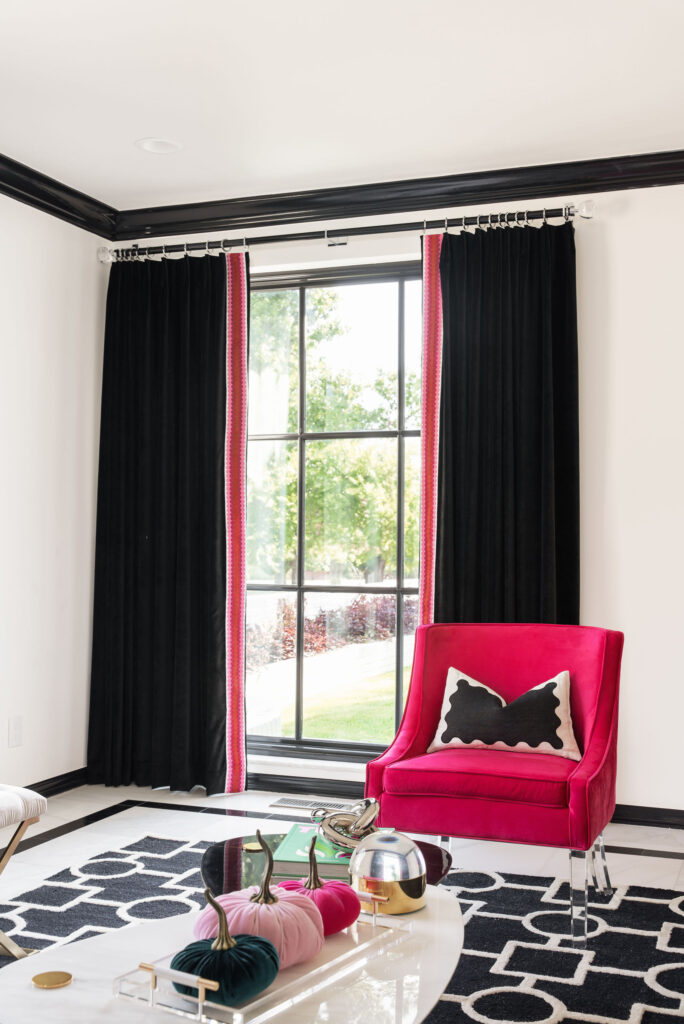 A stylish black and white room with a chic black and white rug, bold black drapery with chair matching trim and featuring a pop of color with a dark pink chair.
