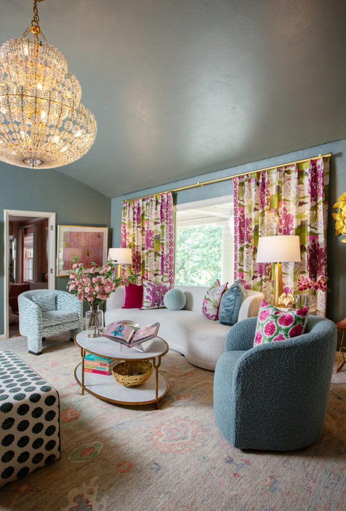 A cozy living room with blue walls, vibrant pink and blue furniture with stunning patterned window treatments creating a cheerful and inviting atmosphere.
